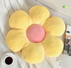 a yellow flower pillow sitting on top of a bed next to a cup of coffee