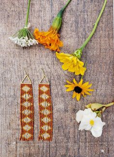 two pairs of beaded earrings sitting on top of a wooden table next to flowers