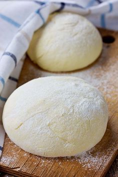 two uncooked round breads on a wooden cutting board with a blue and white towel