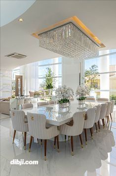 a large dining room table surrounded by white chairs and chandelier in front of windows