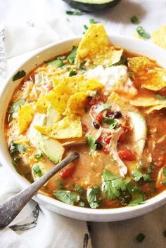 a bowl of soup with tortilla chips and avocado on the side