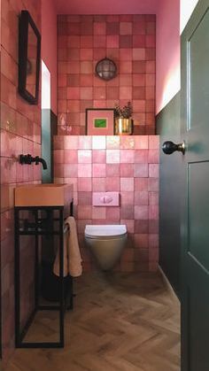 a small bathroom with pink tiles on the walls and wood flooring, along with a toilet