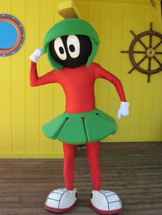 a person in a costume standing on a wooden floor next to a yellow wall and steering wheel