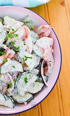 a pink bowl filled with salad sitting on top of a wooden table next to a blue and white towel