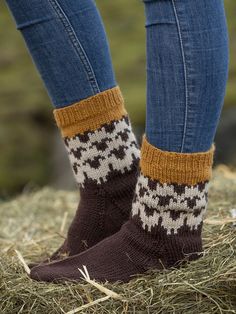 the legs of a woman wearing brown and white knitted socks, standing on hay