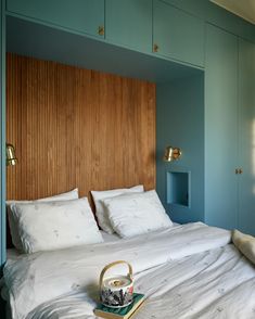 a bed with white sheets and pillows in a room that has blue cabinets on the wall