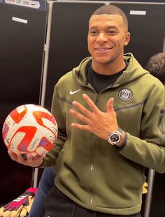 a man is holding a soccer ball in his right hand and smiling at the camera