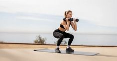 a woman is doing squats on a mat with dumbbells in front of her