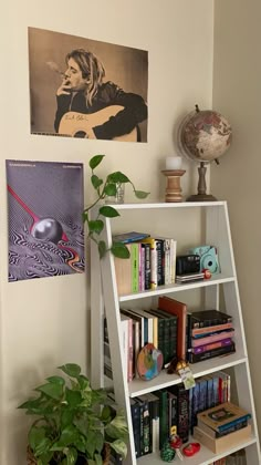 a white book shelf filled with books next to a plant and pictures on the wall