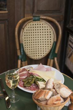 a plate with meat, cheese and bread next to a glass of wine