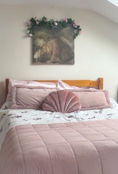 a bed with pink comforter and pillows in a bedroom next to a painting on the wall