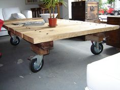 a wooden table with wheels and a potted plant on the top, in a living room