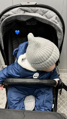 a small child sitting in a stroller wearing a hat and blue coat with a heart on it