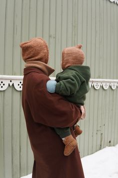 a man holding a child in his arms outside on a snowy day with a barn in the background