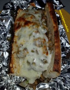 a hot dog covered in cheese and toppings sitting on foil wrapped in tinfoil