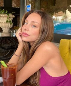 a beautiful woman sitting at a table with a drink in front of her and looking into the distance