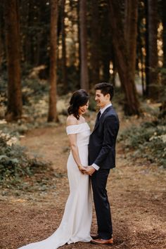 a bride and groom standing together in the woods