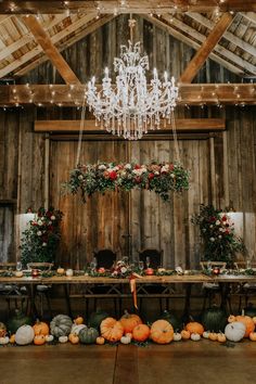 a table with chandelier and pumpkins on it in front of a wooden wall