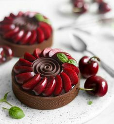 two cakes with chocolate frosting and cherries on a white plate next to each other