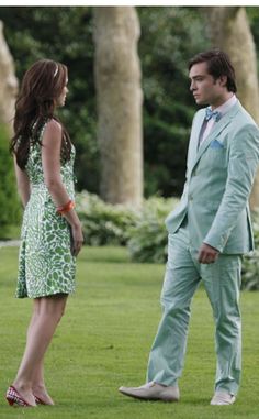 two people standing in the grass talking to each other and one is wearing a green suit