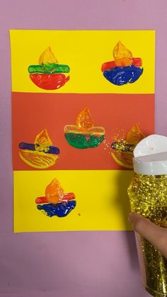 a hand holding a cup with gold glitter in front of a colorful poster on the wall