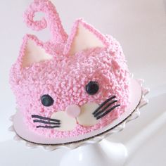 a pink cat cake sitting on top of a white plate with the letter s painted on it