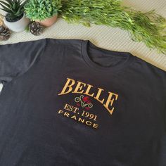 Beauty & The Beast Embroidered T-Shirt The Belle Embroidered T-Shirt brings a touch of Disney magic to your casual wardrobe. This unisex tee features the iconic name 'Belle' embroidered in golden thread, accompanied by a detailed rose design. The embroidery provides a subtle nod to the beloved Beauty and the Beast character while maintaining a versatile, wearable look. Offered in a range of colors, this t-shirt allows you to incorporate the Disney aesthetic into your everyday style. The golden embroidery adds a hint of elegance without being overstated. Whether you're a longtime Disney fan or simply appreciate tasteful designs, this piece makes a stylish statement. Crafted from quality materials, the Belle Embroidered T-Shirt promises long-lasting wear. Its timeless embroidery and relaxed Golden Embroidery, Golden Thread, Disney Tees, Disney Aesthetic, Embroidered Tshirt, Rose Design, Disney Magic, Embroidered Shirt, The Beast