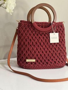 a red handbag sitting on top of a white table next to a vase with flowers