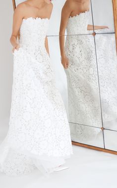 two women in white dresses are looking at their reflection in a mirror and one is holding her hand on her hip