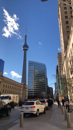 cars are parked on the street in front of tall buildings with a television tower in the background