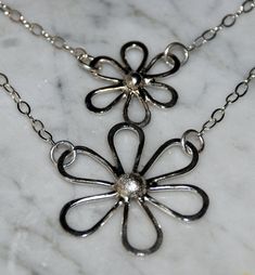 "Delightful Sterling Daisies hand forged from recycled silver are suspended on an 18\" sterling 2 layered chain. The silver petals are hammered for texture and then polished for a high sheen. Large daisy measures 1 1/4\" x 1 1/4\" (30cm x 30cm) and small daisy measures 1\" x 1\" (24 x 24cm). You may choose single small daisy, single large daisy, or the double daisy necklace." Silver Hypoallergenic Flower Pendant Necklace, Hypoallergenic Silver Necklace With Flower Pendant, Hypoallergenic Silver Flower Pendant Necklace, Hand Forged Silver Dainty Necklace, Silver Hypoallergenic Flower Necklace, Silver Flower Pendant Necklace With Soldered Detail, Large Daisy, Layered Chain, Daisy Necklace