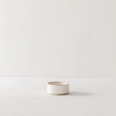 a small white bowl sitting on top of a table next to a wall with a plant in it