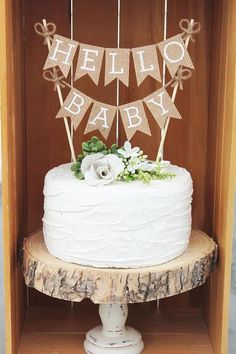 a white cake sitting on top of a wooden table next to a sign that says hello baby