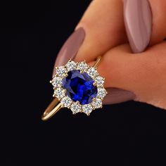 a woman's hand holding a ring with a blue stone surrounded by diamonds