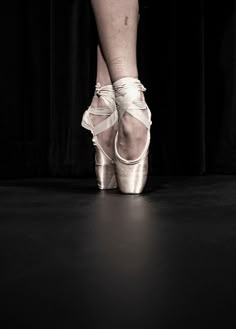 a woman's feet in ballet shoes on a black floor with curtains behind her