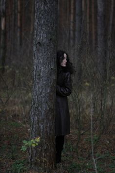 a woman standing in the woods behind a tree