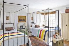 two beds in a bedroom with white walls and wooden floors, one has a colorful blanket on the bed