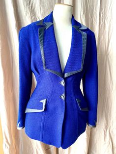 Vintage Thierry Mugler hourglass fitted jacket from the 1980s with shoulder pads, snap buttons, fully lined, curved seams, and functional flap pockets, in a deep purplish blue woven nubby wool. Lapels, cuffs and collar are trimmed in black satin with the iconic space age-y arrow motifs that marked 80s Mugler. Jacket nips in at waist and flares over hip to accentuate the body. In very good vintage condition; no flaws noted but the satin trim has some faint fade. 99% wool + 1% Lycra. Size: Vintage Fitted Royal Blue Blazer For Workwear, Fitted Royal Blue Blazer For Work, Fitted Royal Blue Blazer For Office, Fitted Royal Blue Office Blazer, Fitted Royal Blue Winter Blazer, Retro Fitted Blue Blazer, Fitted Retro Blue Blazer, Fitted Royal Blue Outerwear For Work, Fitted Royal Blue Blazer For Fall