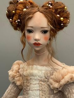 a doll with red hair wearing a dress and pearls on it's head, in front of a gray background