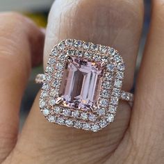 a woman's hand holding an engagement ring with a large pink diamond surrounded by smaller diamonds