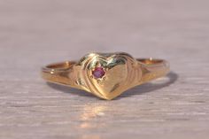 This stunning piece, known as The Heartfelt Ruby, features a captivating natural ruby set at the center of a heart motif. The natural ruby adds a touch of color and elegance, making it a delightful piece for any collection. The ring is crafted in yellow gold and is currently a finger size 4 but can be adjusted to any finger size for an additional charge upon request, ensuring a perfect fit. Love this piece, but don't have the money to spend right now? We offer FREE layaway on every item in our shop. With just 20% down, take one full year (interest-free) to pay off your new jewelry! There are no hidden fees or charges, ever. For more information on our layaway policy, please contact us. Each piece has been hand-selected and meticulously identified and graded by a Graduate Gemologist who has Fine Ruby Heart-shaped Jewelry, Fine Ruby Heart Jewelry, Heart-shaped Ruby Birthstone Jewelry, Ruby Heart Charm Jewelry, Classic Heart Shaped Birthstone Jewelry, Classic Heart-shaped Birthstone Jewelry, Classic Ruby Birthstone Ring For Valentine's Day, Heirloom Heart-shaped Gemstone Ring, Elegant Red Heart Ring In 14k Gold