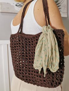 a woman carrying a brown crocheted bag with a scarf on it's shoulder