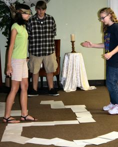 two girls and one boy are standing in front of a cross on the floor with paper