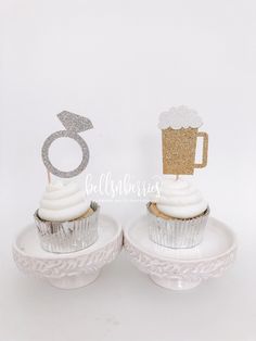 two cupcakes with white frosting and silver decorations on them, one has a beer mug