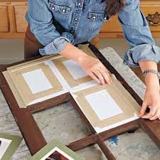 a woman in denim shirt working on framed artwork with wood frame and paintbrushes