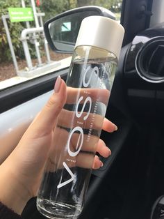 a woman is holding a water bottle in her hand while she sits in the driver's seat