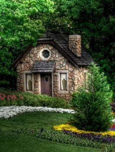 a small stone house surrounded by flowers and trees