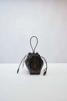 This wristlet bag from Alaïa's Spring/Summer 2024 collection, is made entirely from calfskin leather and laser cut with a New Vienne motif – a perforated circular pattern adapted from the iconic Vienne created by Azzedine Alaïa in 1992. Designer Evening Bucket Bag With Leather Handles, Luxury Handheld Bucket Bag For Evening, Designer Leather Bags With Perforations, Elegant Leather Shoulder Bag With Perforations, Black Evening Bucket Bag With Round Handle, Black Bucket Bag With Round Handle For Evening, Leather Bucket Bag With Detachable Handle For Party, Leather Party Bucket Bag With Detachable Handle, Luxury Evening Bucket Bag With Leather Handles