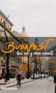 a man riding a bike down a street next to tall buildings with orange lettering on it