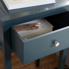 an open drawer on a blue table with a book in the bottom section and a white framed piece of artwork above it